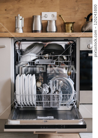Modern kitchen with a dishwasher full of clean plates and utensils. 120243800