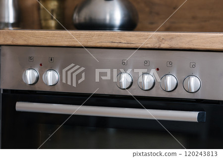 Control panel of an oven with silver knobs in a stylish kitchen. 120243813
