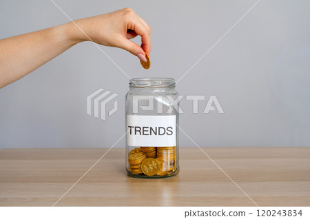 Bank of coins with the inscription Trends and female hand. Investments in popular and relevant topics. New ideological trends of fashion. Recent and latest trend. Business and finance Bank of coins with the inscription Trends and female hand. Investments in popular and relevant topics. New ideological trends of fashion. Recent and latest trend. Business and finance 120243834
