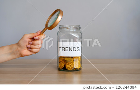 Bank of coins with the inscription Trends and magnifying glass. Analysis popular and relevant topics. New ideological trends of fashion. Recent and latest trend. Business and finance. Investments 120244094