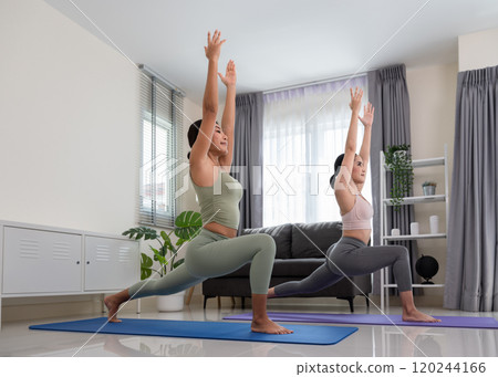 Two women wearing sportive top and leggings doing yoga exercise athome, stretching in Anjaneyasana or High Lunge Pose in living room. Relaxation and Healthcare concept.. 120244166