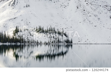 Serene winter landscape of tranquil Bow lake reflecting snow covered mountains and evergreen pine trees in Banff national park, Canada 120244174