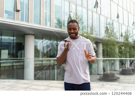 African american man talking on smartphone on street in city outdoor. Man with cell phone chatting with friends. Smiling person making answering call by cellphone. Guy having conversation by mobile 120244406