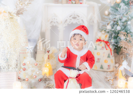 一個微笑的 2 歲孩子穿著聖誕老人服裝，在聖誕樹照片上玩耍 120246538