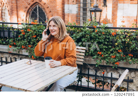 Young charming woman calling with cell telephone while sitting alone on cafe terrace. Female having conversation on mobile phone while rest in cafe 120247891