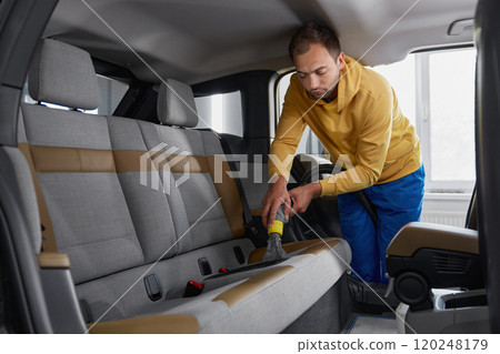 Man car wash service worker vacuuming dust form back passenger seats Man car wash service worker vacuuming dust form back passenger seats 120248179