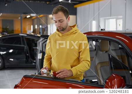 Man brushing leather parts of car door during auto detailing procedure 120248181