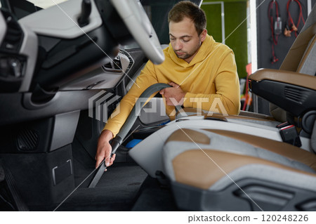 Male master vacuuming car interior from dust using professional equipment 120248226