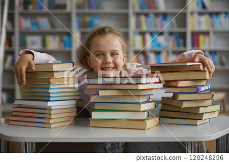 Happy glad little school girl child hugging stack of textbooks in library Happy glad little school girl child hugging stack of textbooks in library 120248296