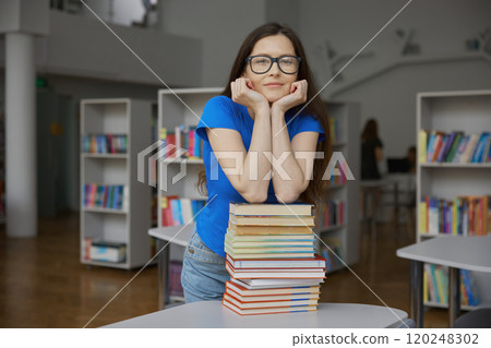 Young woman overloaded with huge stack of paper book standing over bookstore 120248302