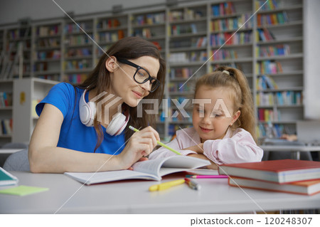 Young woman tutor teaching little girl to read in public library Young woman tutor teaching little girl to read in public library 120248307