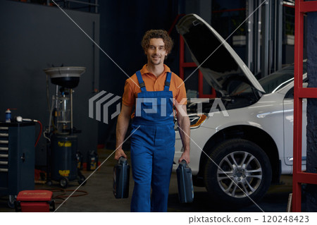Man auto mechanic carrying canisters with car motor oil 120248423