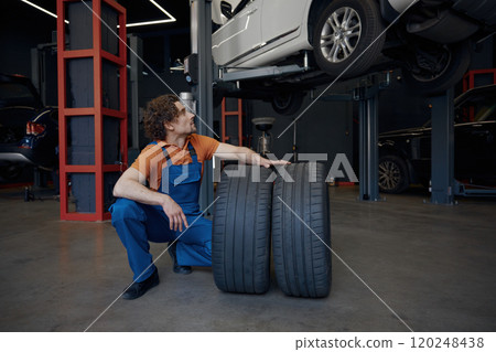 Repairman rolling car spare tires while working on wheel replacement Repairman rolling car spare tires while working on wheel replacement 120248438