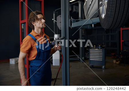 Male auto mechanic using impact wrench during tires replacement Male auto mechanic using impact wrench during tires replacement 120248442