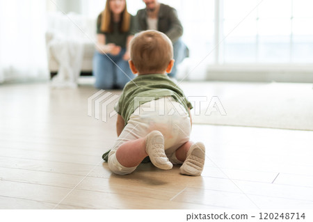 Happy family. Mother father looking at cute little toddler girl crawling on floor in bedroom. Infant baby resting playing with parents indoor at home. Mom dad newborn baby. Cute crawling child 120248714