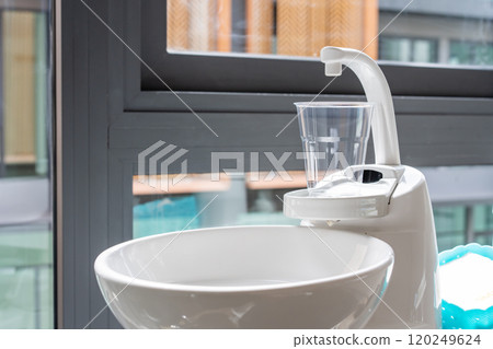 A plastic glass on a cup holder of the modern ceramic mouth cleaning sink in the dentist office near a window, A plastic glass on a cup holder of the modern ceramic mouth cleaning sink in the dentist office near a window, 120249624