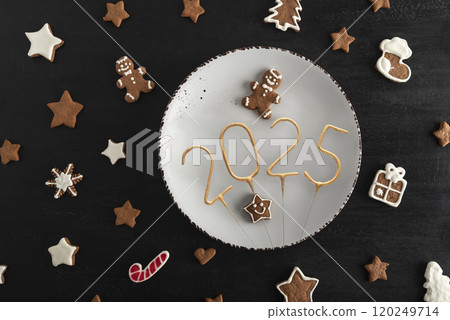 Top view Tasty glazed painted cookies on white plate: numbers 2025, stars and fir-tree. New Year food concept Top view Tasty glazed painted cookies on white plate: numbers 2025, stars and fir-tree. New Year food concept 120249714