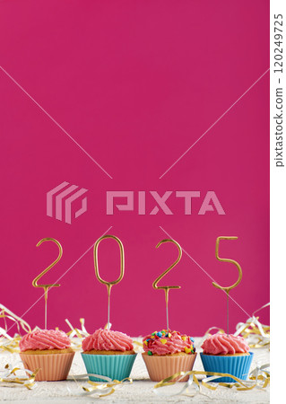 New Years background. Holiday cupcakes with numbers 2025 surrounded by New Years tinsel on pink background. Vertical frame. Copy space. 120249725