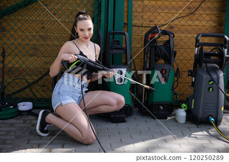 A Young Woman Enthusiastically Using a Pressure Washer in a Bright Outdoor Setting A Young Woman Enthusiastically Using a Pressure Washer in a Bright Outdoor Setting 120250289