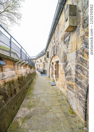 Visitors stroll through the ancient stone pathways of Konigstein Fortress in Saxony, admiring its impressive architecture and rich history on a cloudy day. 120250982