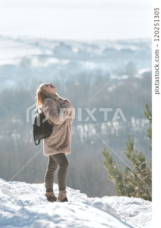 Full-length portrait of young cheerful woman walking in nature on sunny winter day against of hills. Vertical frame. 120251305