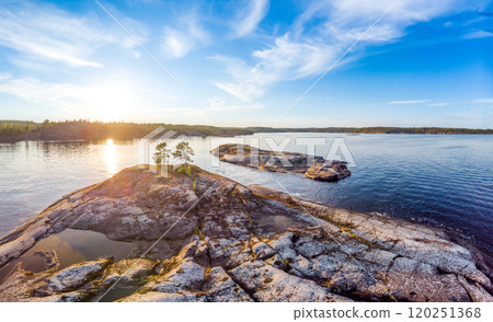 Aerial top view to island overgrown with sparse trees in summer sunny day. Skerries Ladoga lake consisting of 650 rocky islands and steep cliffs. National park, Karelia, Russian nature. Aerial top view to island overgrown with sparse trees in summer sunny day. Skerries Ladoga lake consisting of 650 rocky islands and steep cliffs. National park, Karelia, Russian nature. 120251368