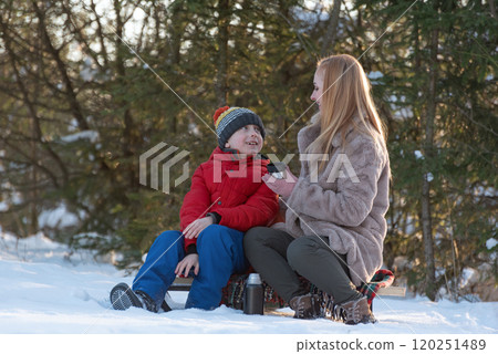 Young woman with son in snowy forest on picnic drink hot tea. Happy childhood. Winter time. Young woman with son in snowy forest on picnic drink hot tea. Happy childhood. Winter time. 120251489