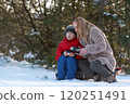 Mother and child spending time outdoors in winter. Woman pours hot tea from thermos into mug. 120251491