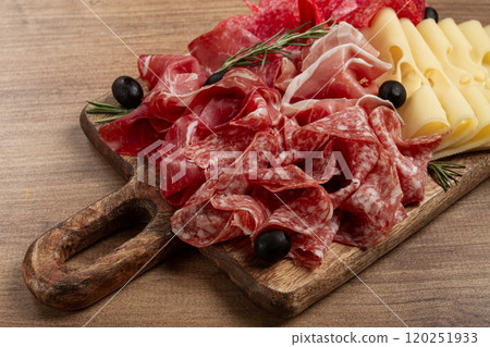 Assorted meat, appetizer, prosciutto, salami and ham, with maasdam cheese and olives, on a wooden board, breakfast, top view, close-up, no people Assorted meat, appetizer, prosciutto, salami and ham, with maasdam cheese and olives, on a wooden board, breakfast, top view, close-up, no people 120251933