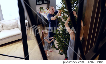 A young family creates a warm and festive atmosphere in their living room by decorating the Christmas tree with Christmas tree decorations. Preparing for Christmas with the family A young family creates a warm and festive atmosphere in their living room by decorating the Christmas tree with Christmas tree decorations. Preparing for Christmas with the family 120251984