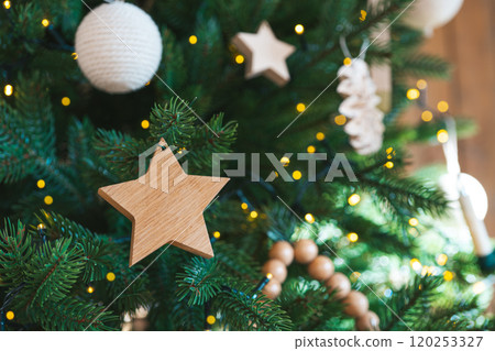 Decorated Christmas tree branch with wooden star and balls on warm lights background Decorated Christmas tree branch with wooden star and balls on warm lights background 120253327