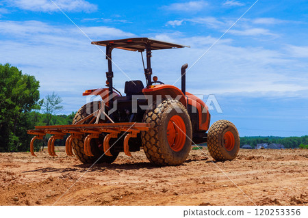 Tractor equipped with tiller is working soil in large, open field under bright blue sky landscape is ready for upcoming planting activities. 120253356