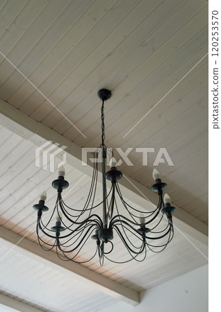 A black wrought iron chandelier under a wooden ceiling painted with white paint. Chalet-style house 120253570