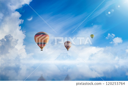 Hot air balloons rising above serene sea, light from heaven, white clouds reflected in water. 120253764