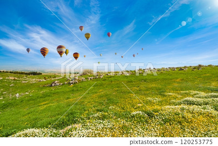 Hot air balloons fly in blue sky over green hills near Denizli, Turkey. 120253775