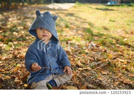 Adorable child in blue hooded sweater sitting outdoors on autumn day Adorable child in blue hooded sweater sitting outdoors on autumn day 120253923