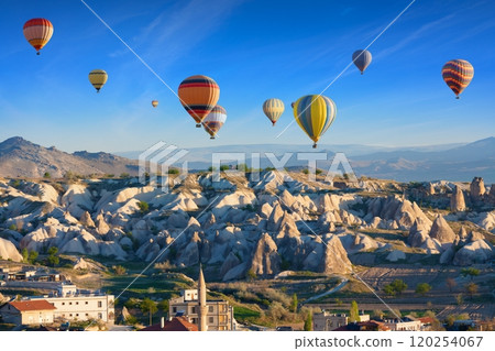 Colorful hot air balloons fly in blue sky over amazing rocky valley in Cappadocia, Turkey. 120254067