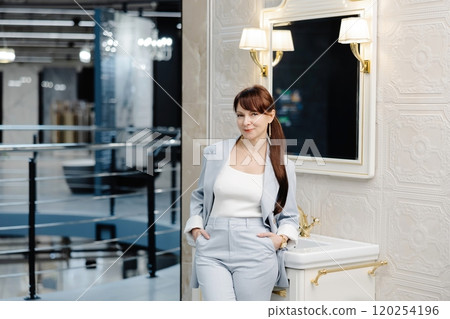 Woman in blue suit adjusts faucet in showroom bathroom 120254196