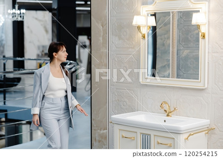 Woman in light suit stands near a freestanding bathtub in a modern showroom 120254215