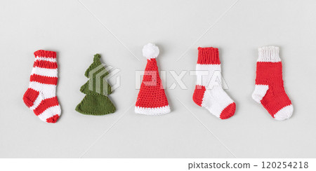 Knitted Christmas toys in form of red and white socks, Santa Claus hats, green Christmas trees on gray background. Top view, flat lay. 120254218