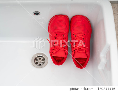A pair of vibrant red sneakers placed inside a white sink, ready for cleaning and freshening up. A pair of vibrant red sneakers placed inside a white sink, ready for cleaning and freshening up. 120254346