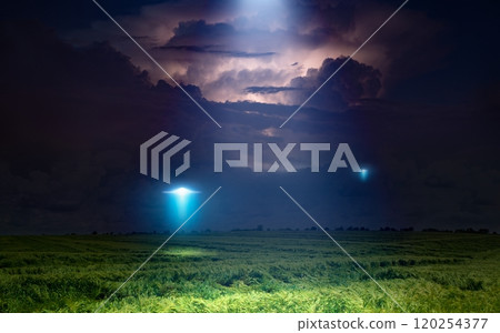 Scenic sci-fi image: UFO or alien spacecraft  inspect green grass field with bright spotlight in dark stormy night sky 120254377