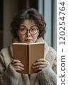 A woman wearing glasses reading a book. 120254764