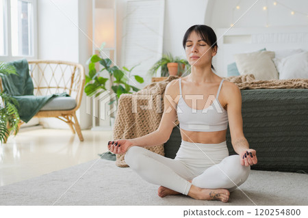 Yoga mindfulness meditation. Young healthy woman practicing yoga in living room at home. Woman sitting in lotus pose meditating smiling relaxing indoor. Girl doing breathing practice. Yoga at home Yoga mindfulness meditation. Young healthy woman practicing yoga in living room at home. Woman sitting in lotus pose meditating smiling relaxing indoor. Girl doing breathing practice. Yoga at home 120254800