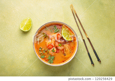 Tom yum soup with shrimps, lime, chili pepper and cilantro is served in bowl with chopsticks, traditional Thai cuisine 120256429