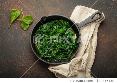 Healthy steamed spinach in cast iron pan on brown rustic background top view 120256430