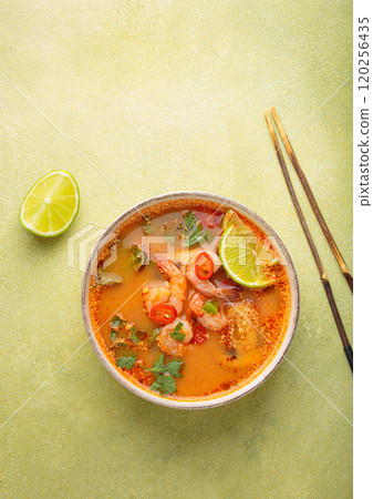 Tom yum soup with shrimps, lime, chili pepper and cilantro is served in bowl with chopsticks, traditional Thai cuisine Tom yum soup with shrimps, lime, chili pepper and cilantro is served in bowl with chopsticks, traditional Thai cuisine 120256435