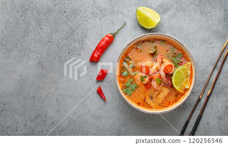 Spicy tom yum soup with shrimps, lime, chili pepper and coriander served in bowl top view, traditional Thai cuisine 120256546