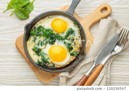 Healthy spinach omelette with two fried eggs in cast iron pan top view 120256547