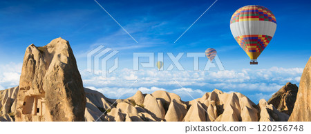 Serenity in skies: hot air balloons over rocky landscape and clouds Serenity in skies: hot air balloons over rocky landscape and clouds 120256748